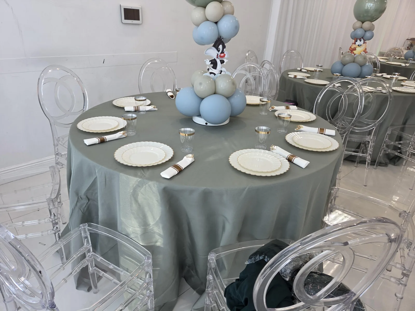 Round banquet table with sage-green linen, clear phoenix chairs and gold-rimmed place settings at a South Florida party